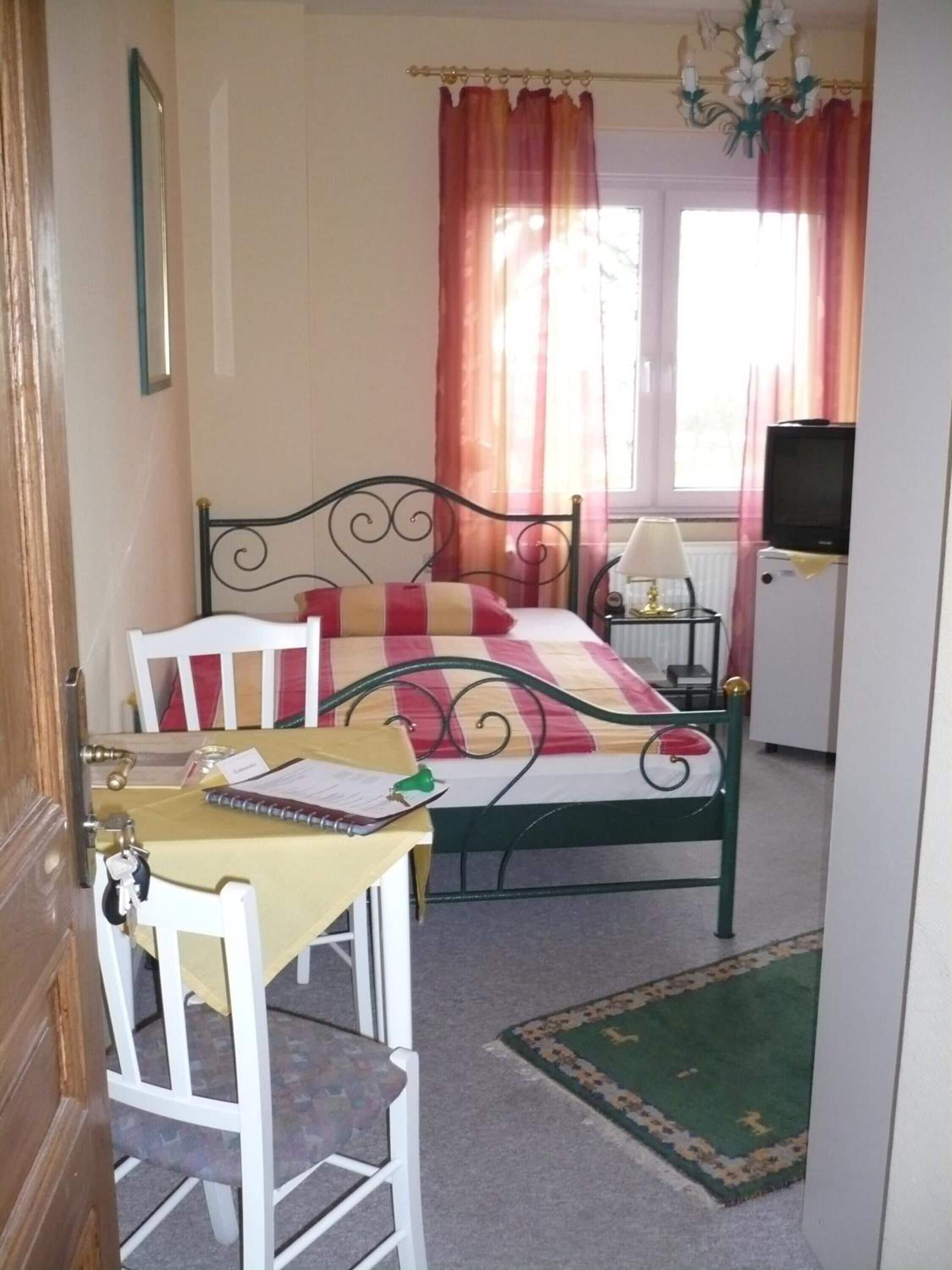 A bedroom with a bed, a desk with a chair, a television, and a window with curtains.