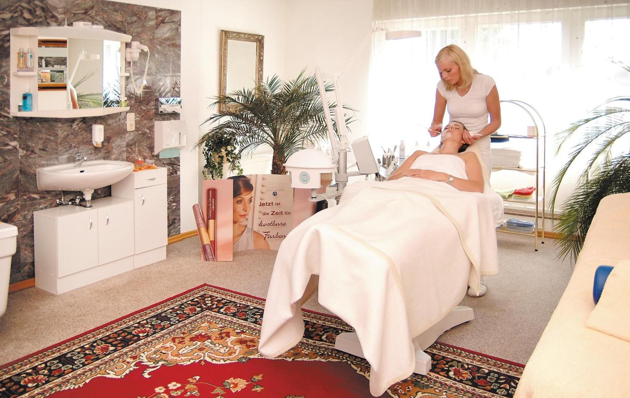 A spa room with a massage table, a sink, a mirror, and a plant.