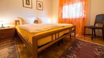 A bedroom with a wooden bed, two bedside tables, a chair, and a window with orange curtains.