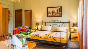 Una habitación de hotel con cama, lámparas de noche, un cuadro en la pared y un florero sobre la mesita de noche.