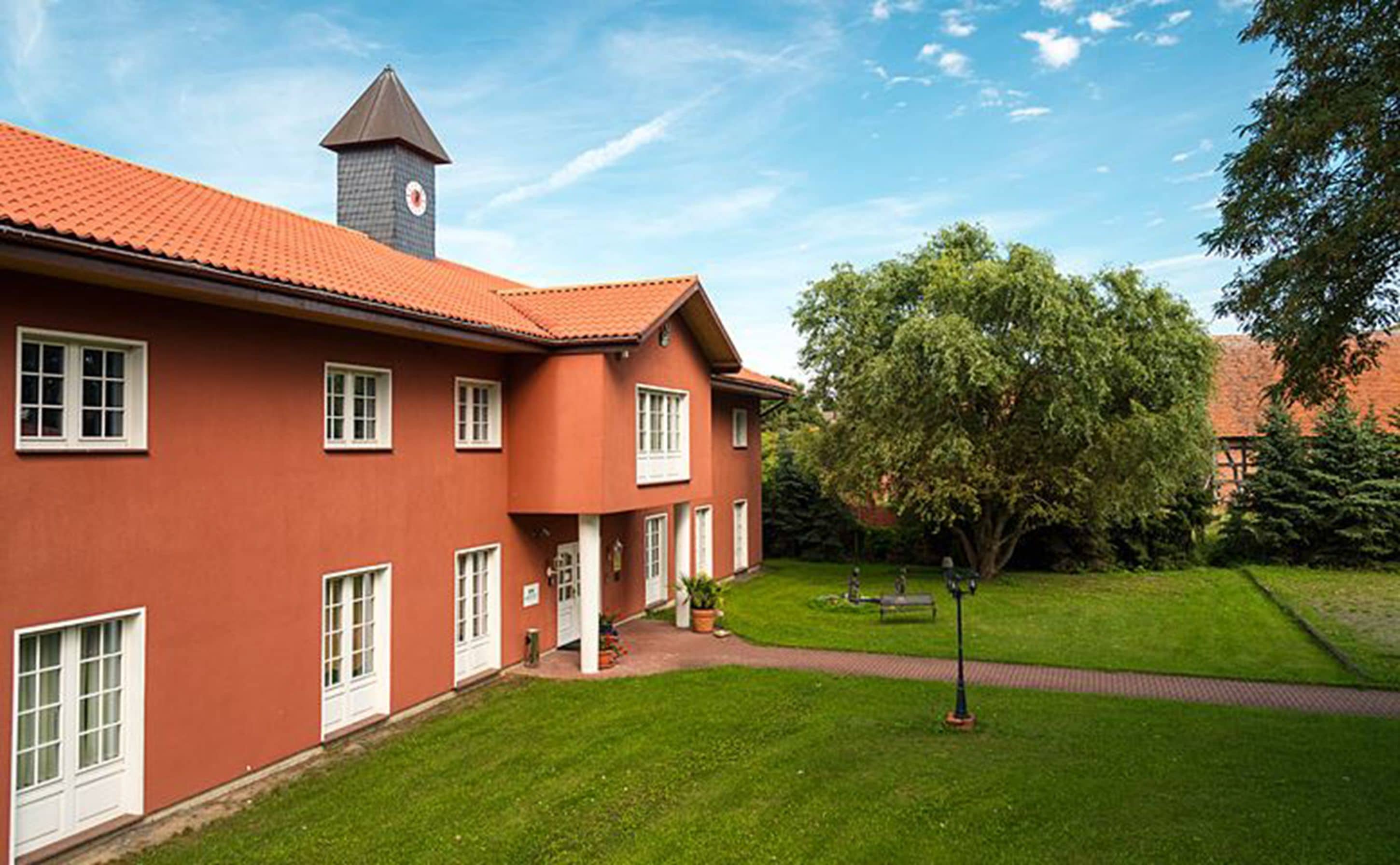 A red building with a clock tower, a well-maintained lawn, and a pathway.