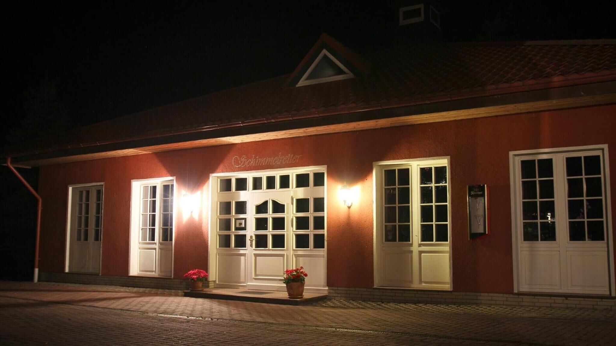 Un edificio con fachada roja, puertas y ventanas blancas, y luces que iluminan la entrada.