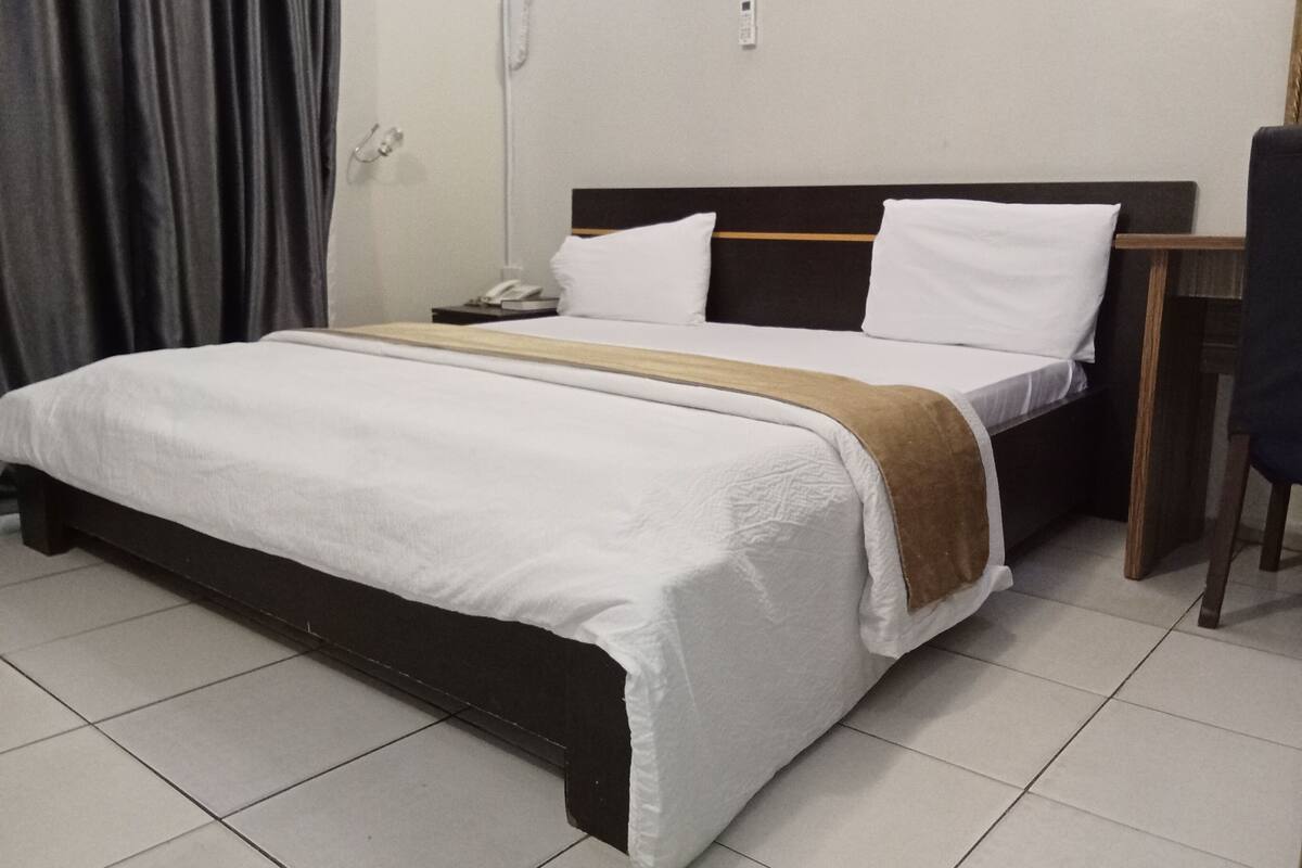 A hotel room with a bed, a bedside table, a chair, and a curtain.