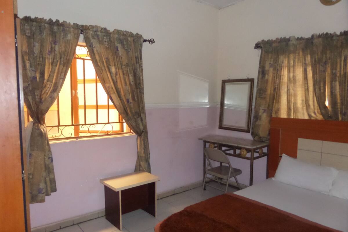 A bedroom with a bed, a desk, a chair, and a window with curtains.