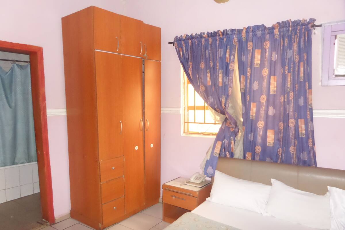 A bedroom with a bed, a wardrobe, a nightstand, and a window with curtains.
