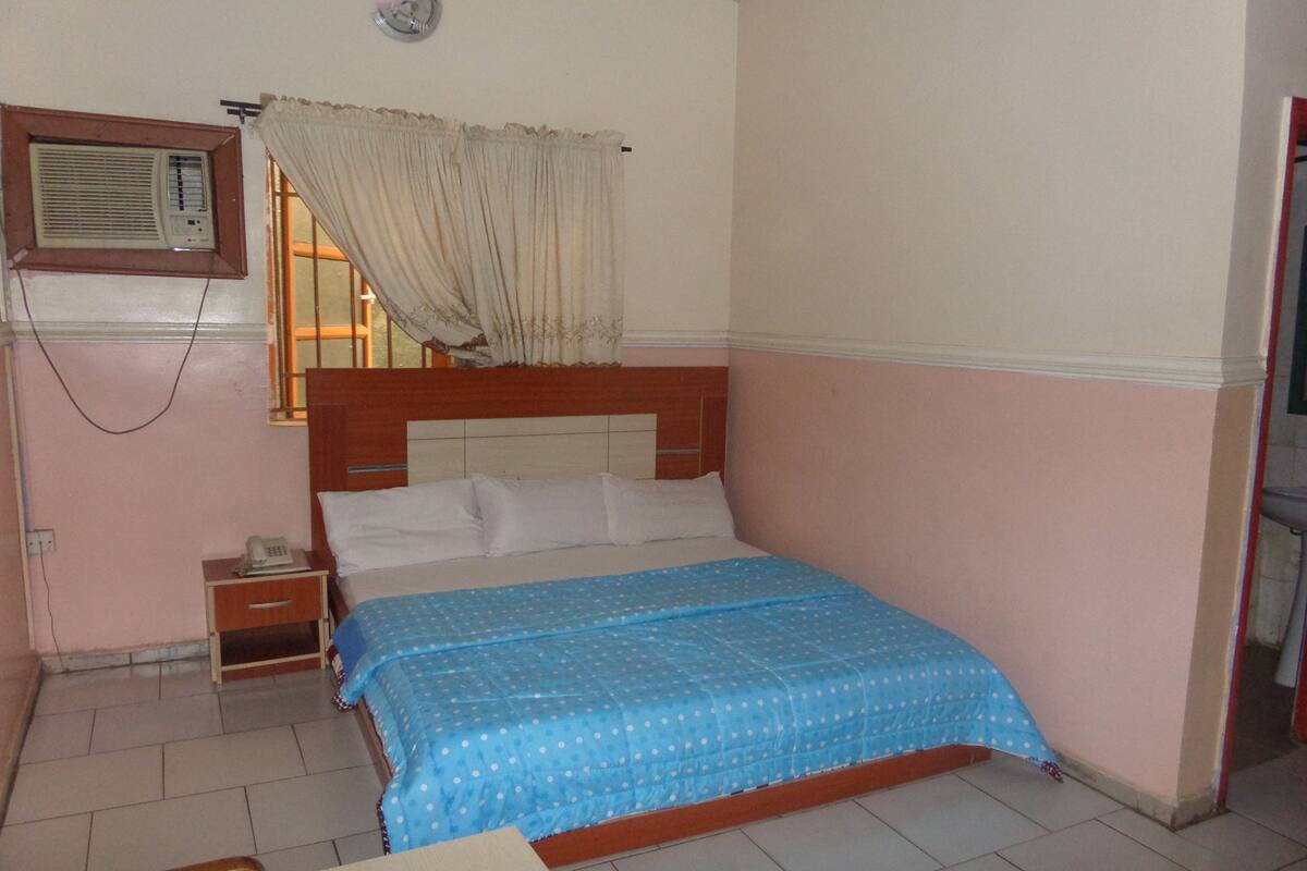 A bedroom with a bed, a nightstand, a telephone, and a window with curtains.
