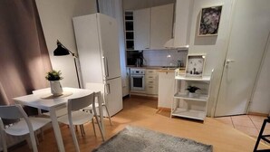 Une cuisine compacte avec des meubles blancs, un coin repas comprenant une table et des chaises, et un tapis gris sur le sol.