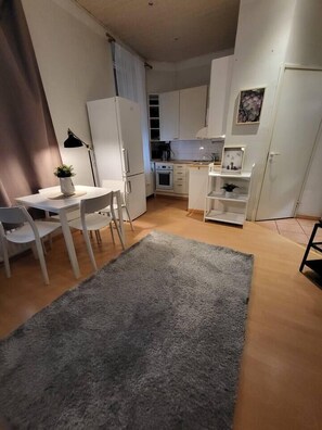 Een kleine keuken met witte kasten, een eethoek met een tafel en stoelen, en een grijs vloerkleed.