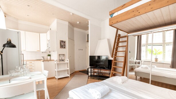 Une chambre d’hôtel moderne équipée d’un lit, d’une télévision, d’une table à manger avec des chaises, d’un coin cuisine et d’une fenêtre donnant sur un paysage agréable.