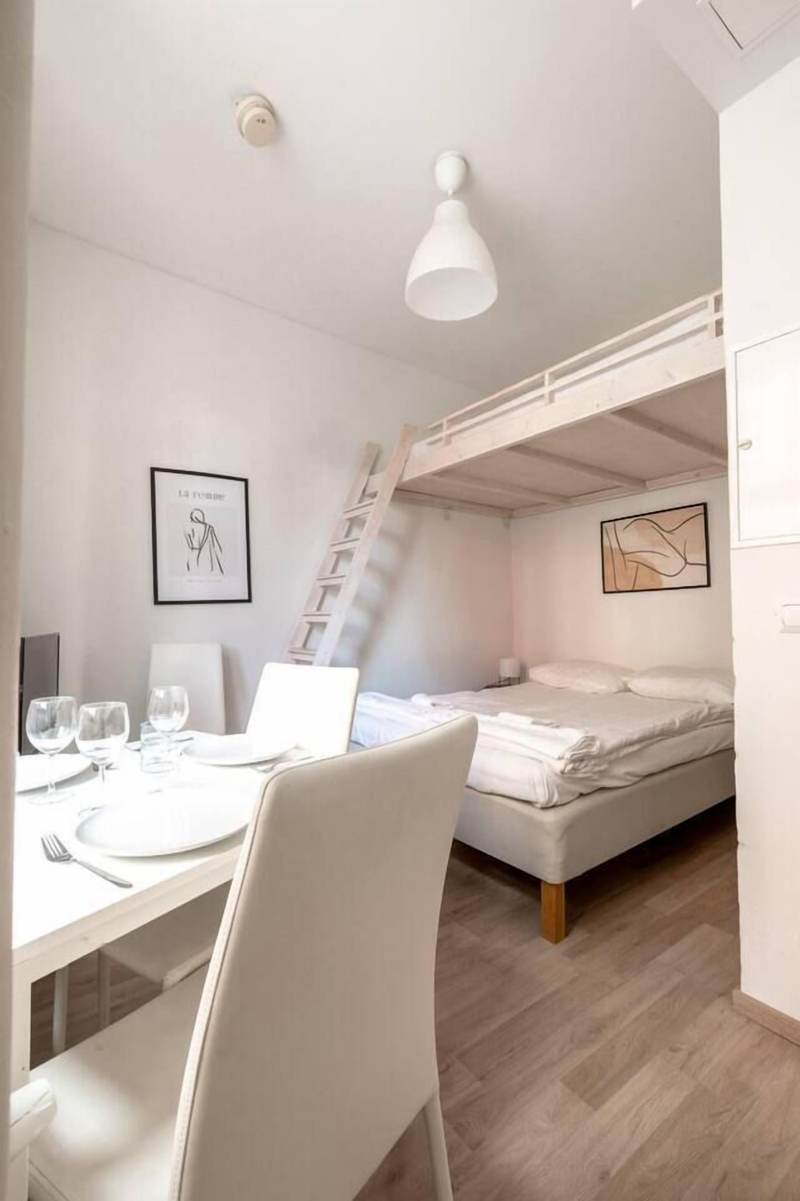 Une petite pièce comprenant un lit superposé, un bureau avec une chaise, un ordinateur portable et un tableau encadré accroché au mur.