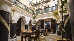 A spacious interior with a high ceiling, ornate columns, and a central seating area with a table and chairs. - Riad Ben Tachfine (Marrakech)