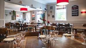 Un restaurante con mesas y sillas de madera, luces colgantes rojas y un menú en una pizarra en la pared.