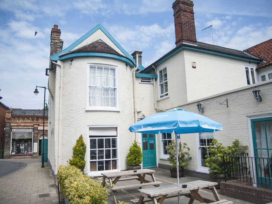 A white building with a blue roof, a green door, and a blue umbrella.