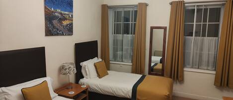 Habitación de hotel con dos camas, un cuadro en la pared, una araña y una ventana con cortinas.
