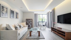 Una sala moderna con un sofá, una mesa de centro de vidrio, un televisor de pantalla plana y un comedor con una mesa y sillas.