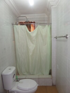 A bathroom with a toilet, a shower curtain, and a tiled wall. - Avery Hotel (Abuja)