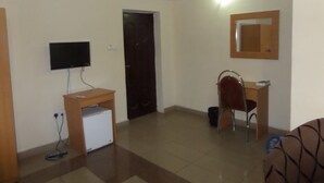 A room with a television mounted on the wall, a desk with a chair, a small refrigerator, and a door. - Avery Hotel (Abuja)