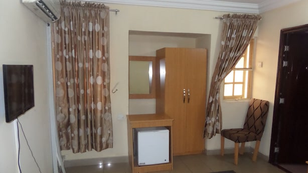 A bedroom with a wardrobe, a small TV, a chair, and a bed. - Avery Hotel (Abuja)