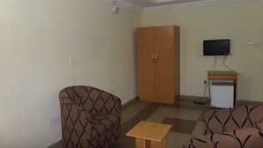 A living room with patterned sofas, a wooden wardrobe, a television on a stand, and a small table. - Avery Hotel (Abuja)