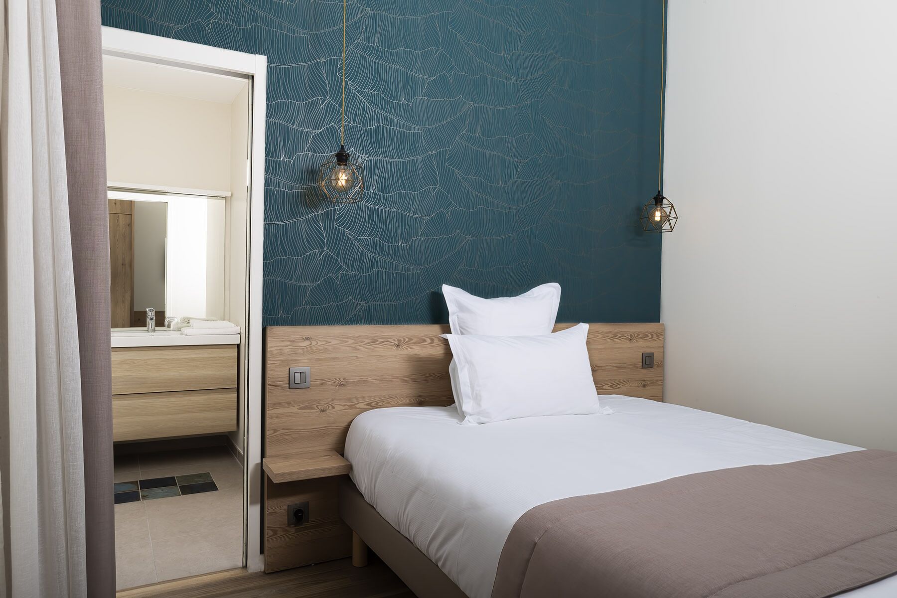 A bedroom with a bed, a nightstand, a mirror, and a wall with a leaf pattern.