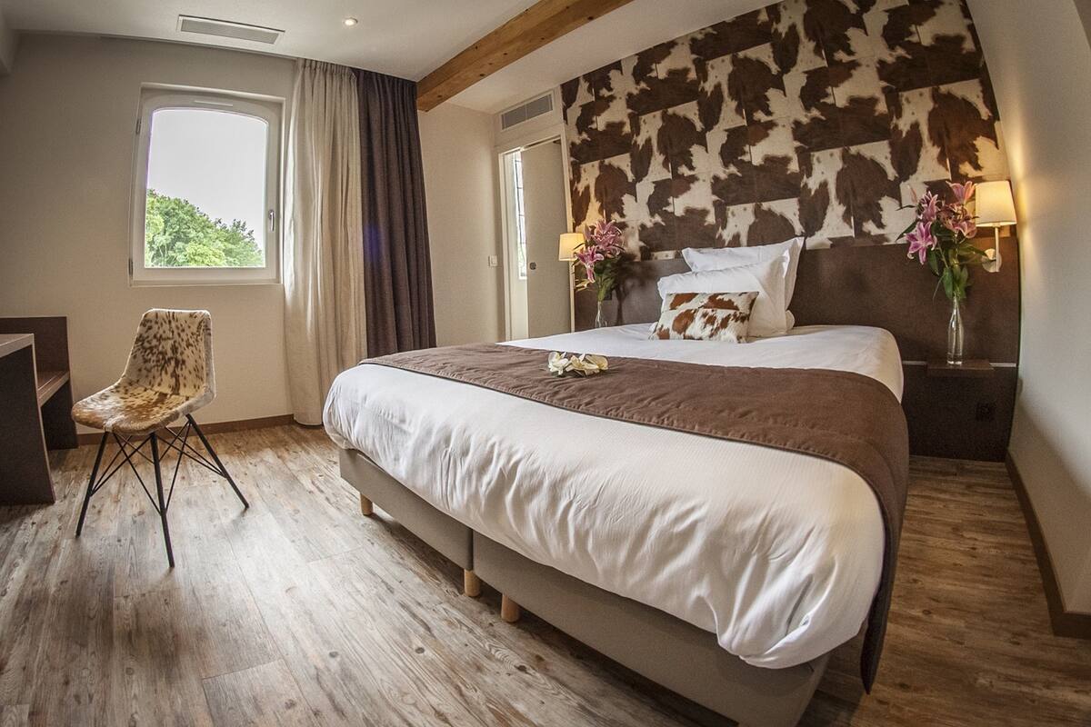 Un dormitorio con una cama grande, una silla, un ventanal y un cabecero con estampado de piel de vaca.