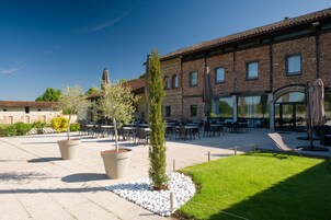 Un patio al aire libre con mesas y sillas, plantas en macetas y un edificio con techo de tejas al fondo.