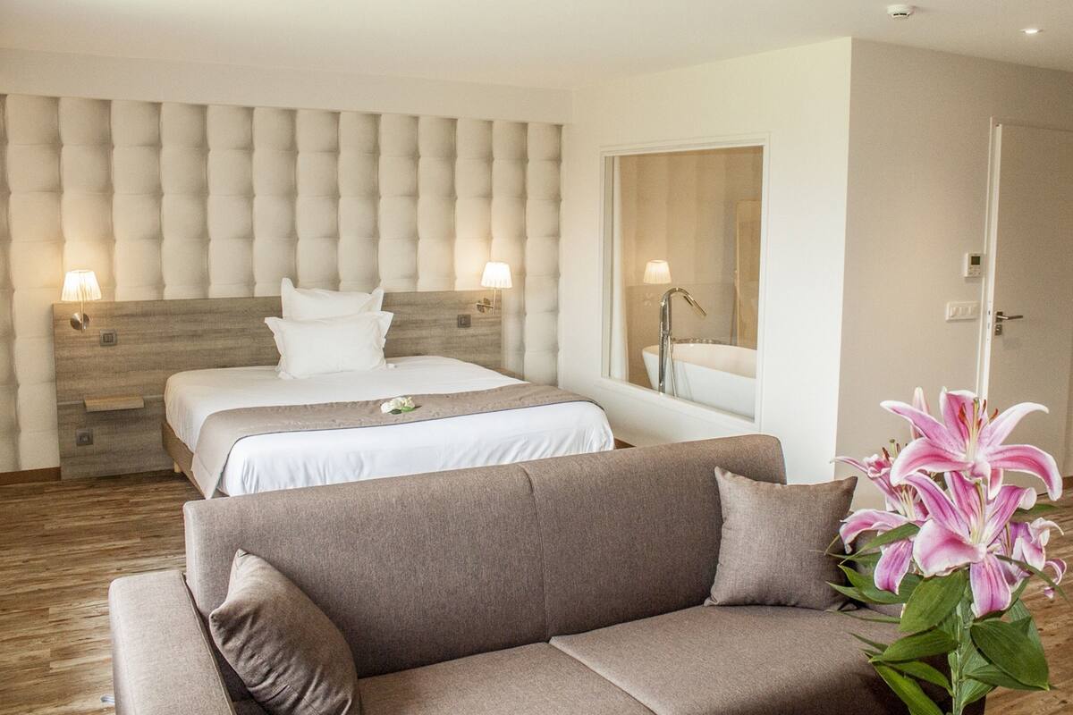 Una habitación de hotel con una cama grande, un sofá, un espejo y una planta en maceta.