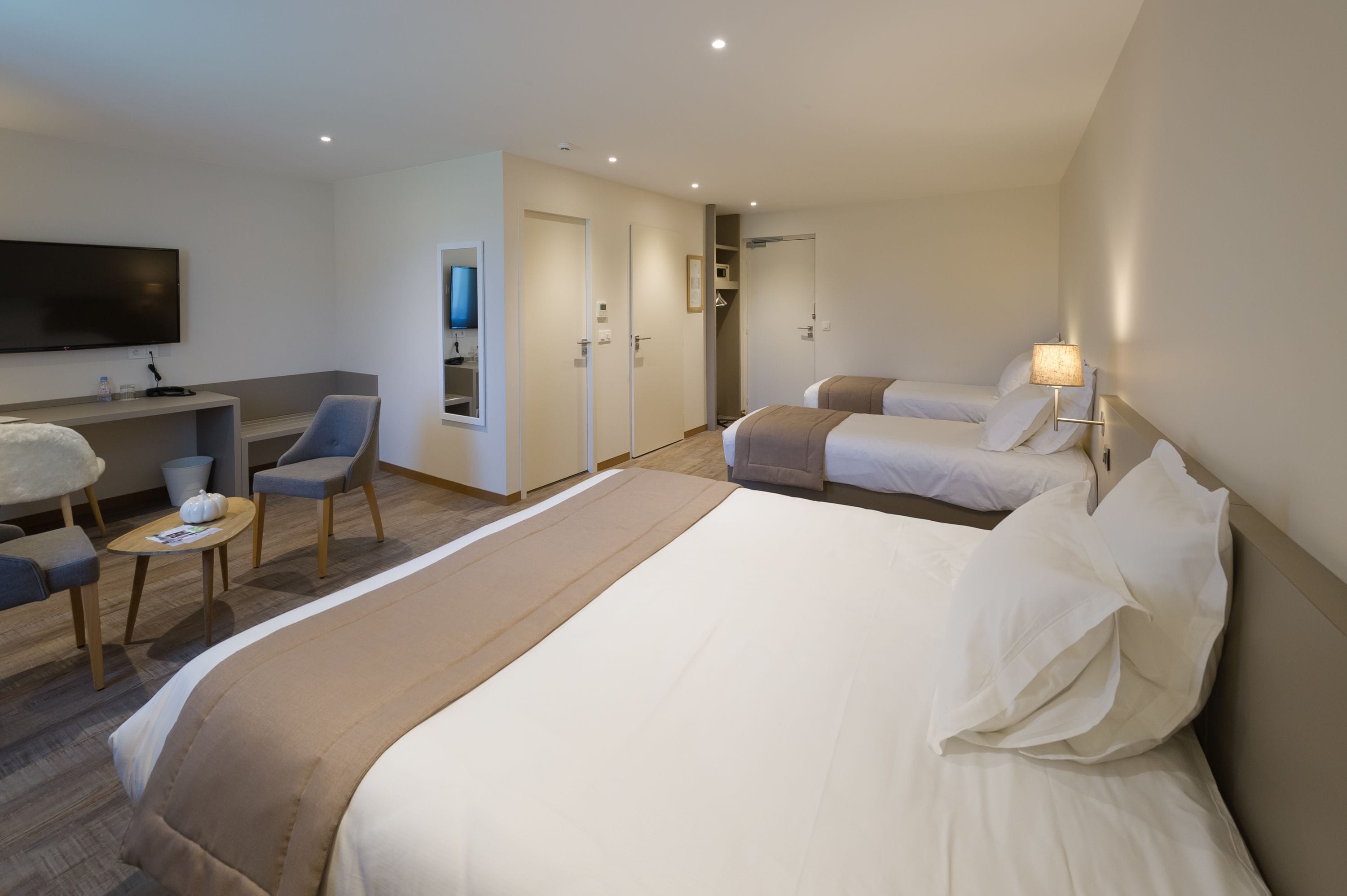 Habitación de hotel con una cama grande, dos camas individuales, un escritorio con silla, un televisor y un mueble para la televisión.