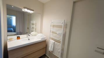 A modern bathroom with a white vanity, a large mirror, and a towel rack.