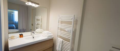 A modern bathroom with a white vanity, a large mirror, and a towel rack.