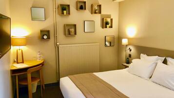 A hotel room with a bed, bedside table, lamp, desk, chair, and wall-mounted mirrors.