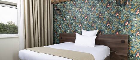 A bedroom with a bed, curtains, a wooden headboard, and a wall with a floral pattern.