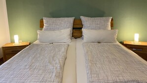 A double bed with a white and grey patterned bedspread, two white pillows, and a wooden headboard. There are two bedside tables with lamps on either side of the bed. - Vacation apartment Schlei - Ferienhof Röhling between Schlei and Baltic Sea (Kappeln)