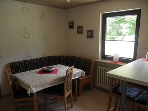 A dining area with a table, chairs, a bench, and a window with a view of trees.