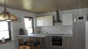A kitchen with a wooden ceiling, white cabinets, a microwave, a stove, and a sink. - Vacation apartment Schlei - Ferienhof Röhling between Schlei and Baltic Sea (Kappeln)