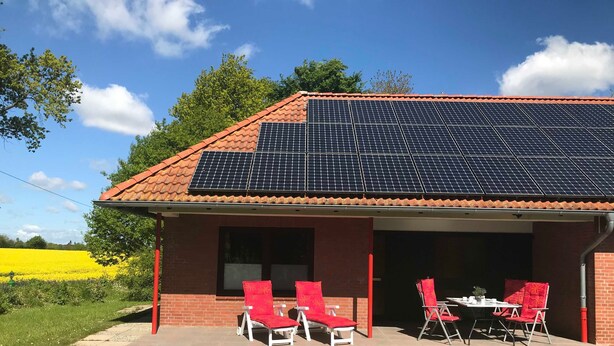 A house with a solar panel roof, a covered patio with red chairs, and a field of yellow flowers in the background. - Vacation apartment Schlei - Ferienhof Röhling between Schlei and Baltic Sea (Kappeln)
