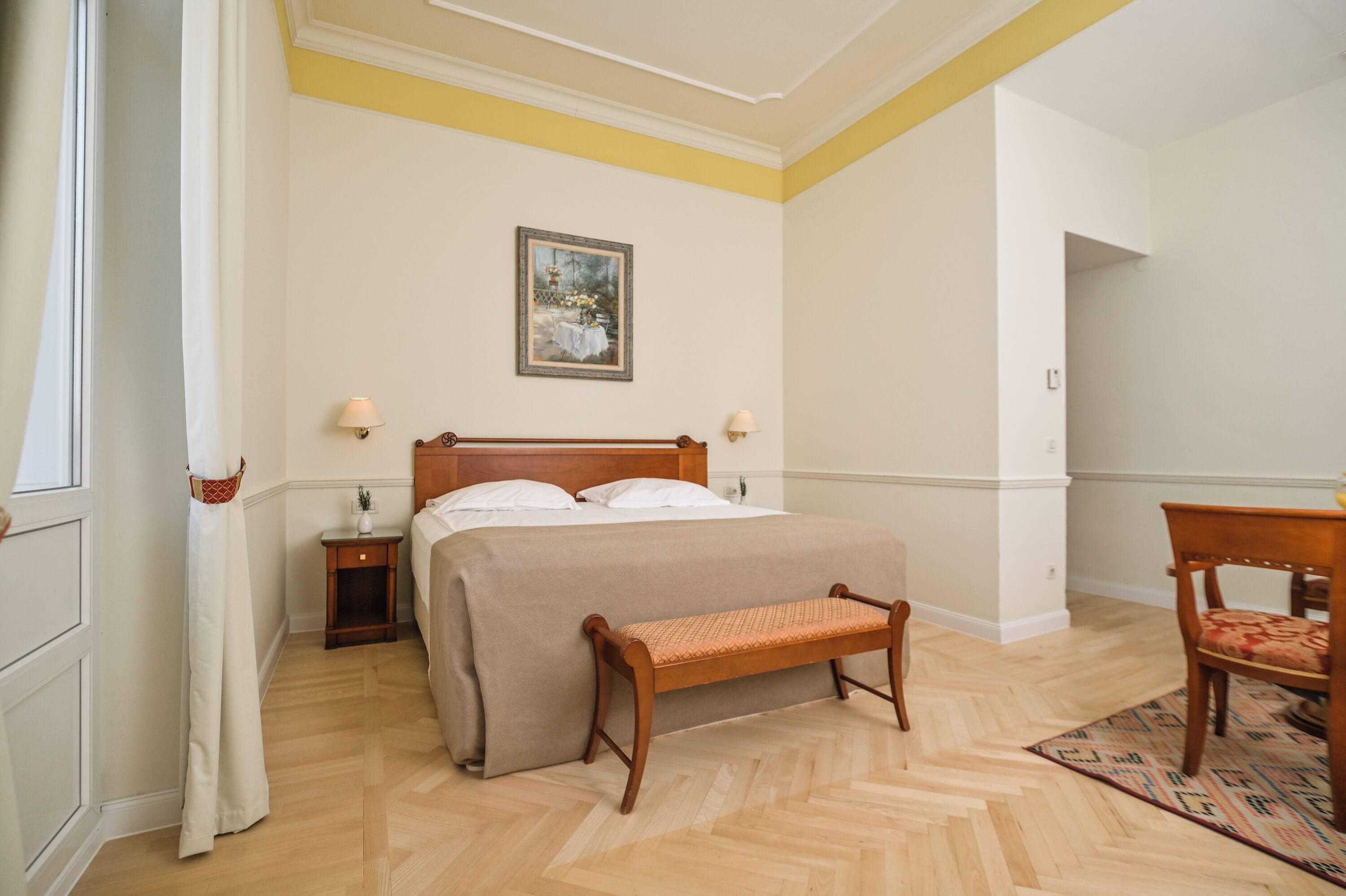 Un dormitorio ordenado con una cama grande, un banco, una mesita de noche y una silla.