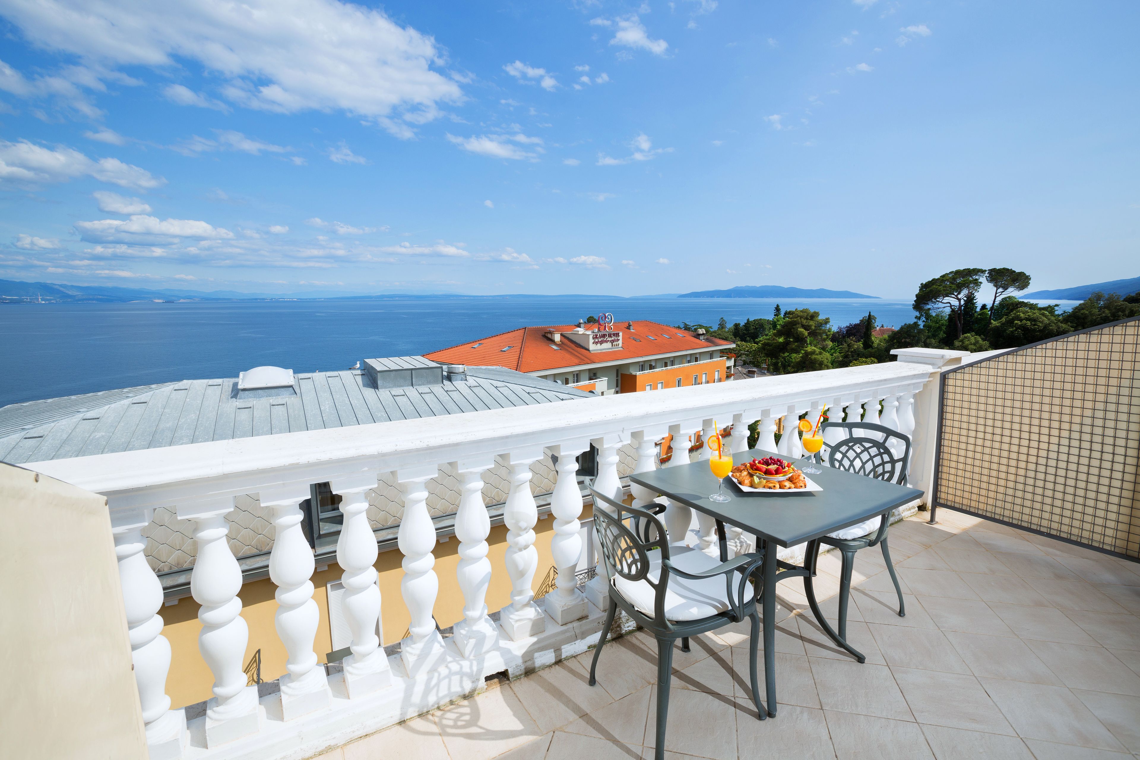 A balcony with a table and chairs, overlooking a scenic view of the sea and distant mountains.