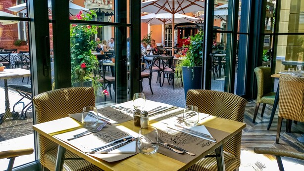 Un café en plein air avec des tables et des chaises, de grands parasols et des plantes en pot.