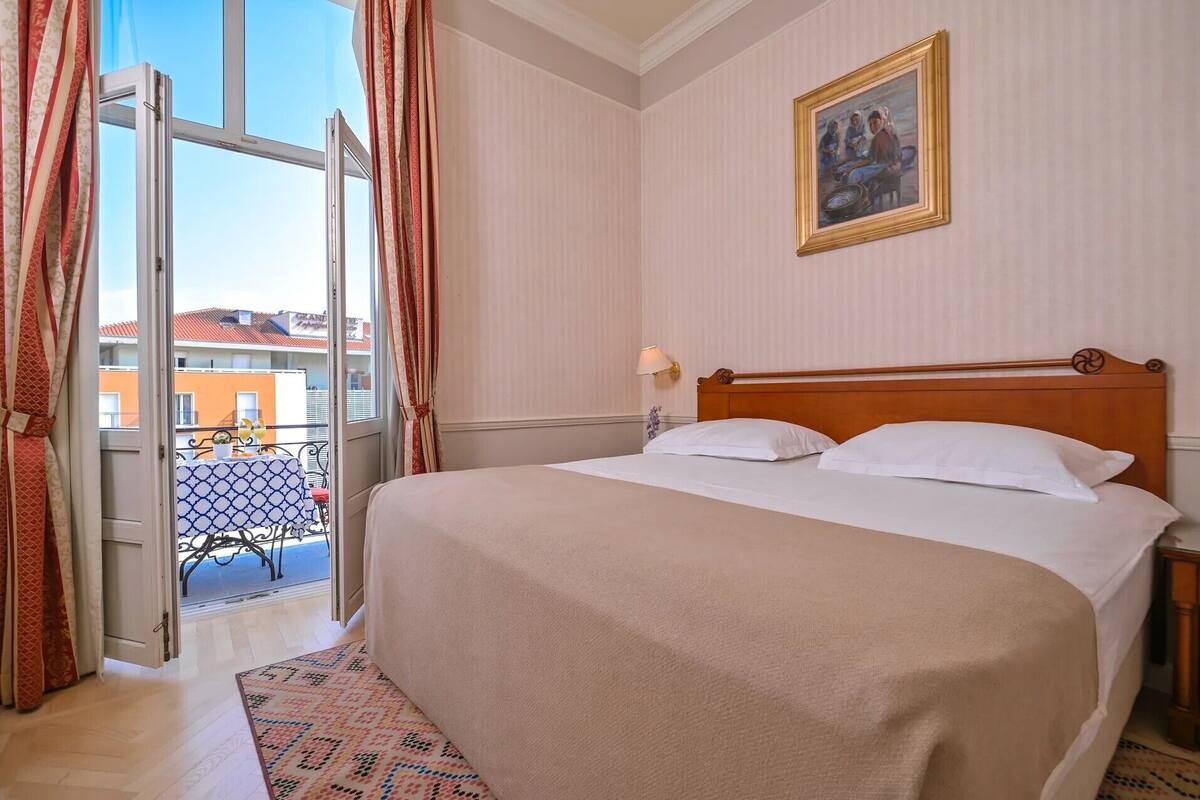 Ein Hotelzimmer mit Bett, einem Gemälde, einem Nachttisch und Blick auf den Außenbalkon.