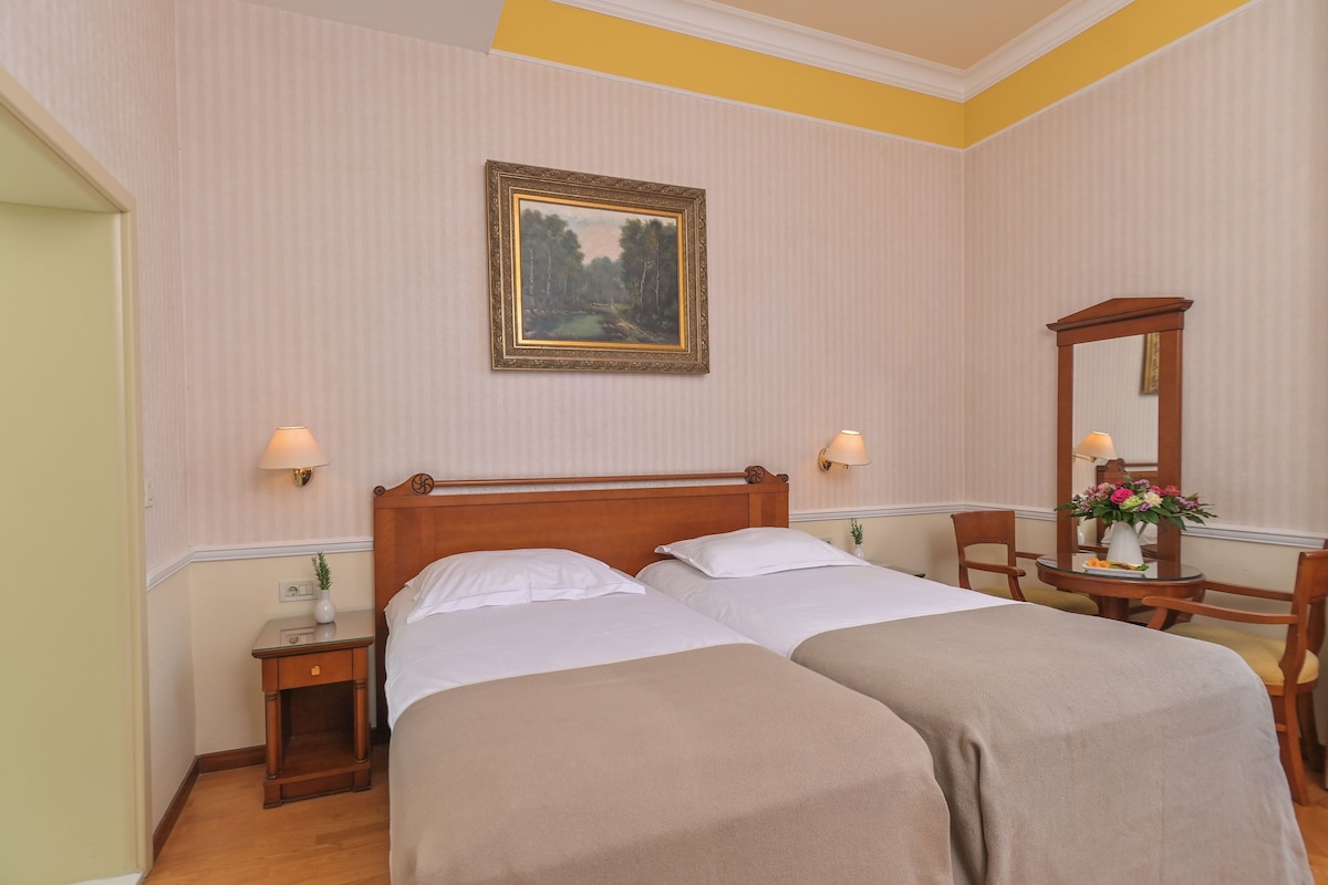A hotel room with two beds, a wooden headboard, a framed painting, a desk with a mirror, and a vase with flowers.