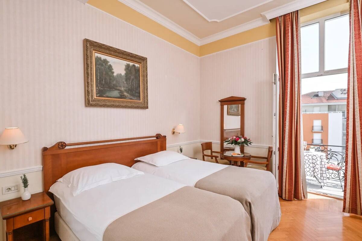 Ein Hotelzimmer mit zwei Betten, einem Schreibtisch mit Stuhl, einem Spiegel und einem Balkon mit Geländer.