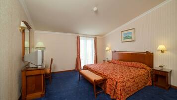 A hotel room with a bed, a desk with a computer, a chair, a bench, and two bedside lamps.