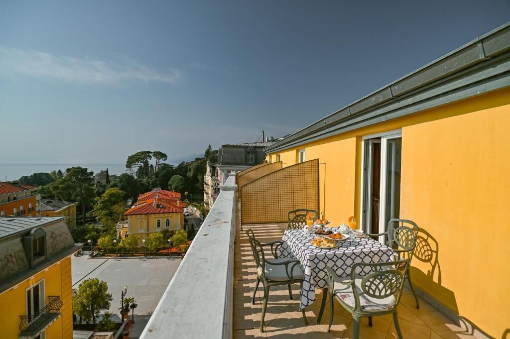Un balcone con tavolo apparecchiato per consumare un pasto, con vista su un panorama urbano di edifici e alberi.
