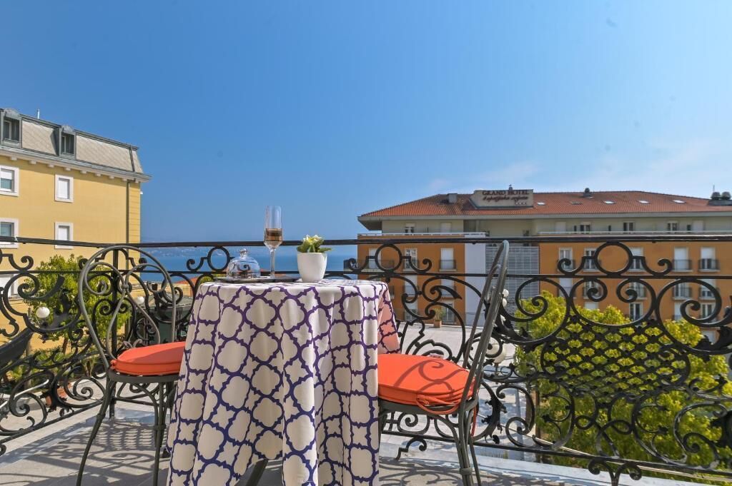 Ein Balkon mit Tisch und Stühlen, der auf ein Gewässer und Gebäude blickt.
