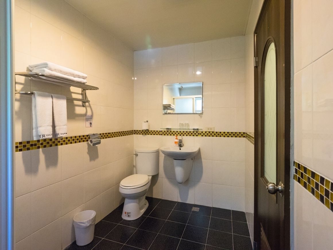 A bathroom with a toilet, sink, and mirror. There is a towel rack with folded towels and a trash bin.