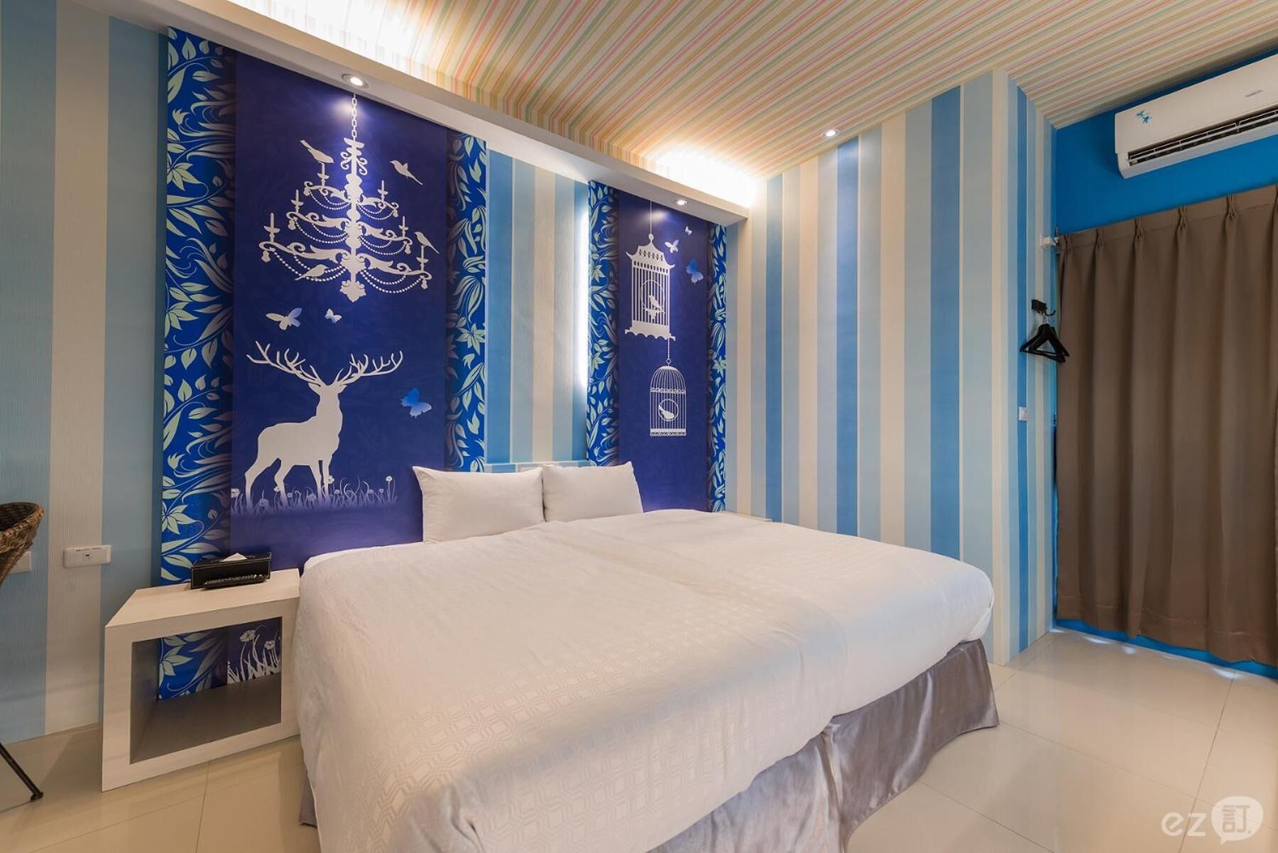 Un dormitorio con cama, mesita de noche y papel tapiz azul y blanco a rayas.