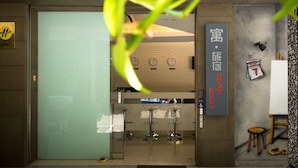 L’entrée d’un hôtel, avec une porte en verre, un comptoir d’accueil et une horloge murale.