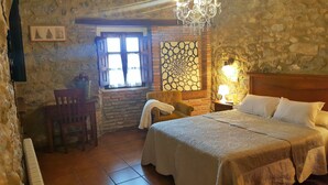 A cozy room with a bed, a chair, a table, and a window with curtains.