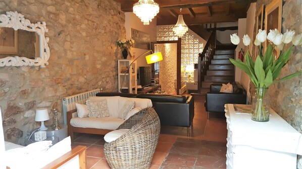 A cozy living room with stone walls, a wicker sofa, a black armchair, and a white coffee table. - El Juacu (Llanes)